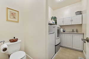 Laundry room featuring a sink, light tile patterned floors, washing machine and dryer, and toilet.