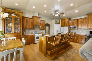 Kitchen with decorative backsplash, under cabinet range hood, white appliances, and ceiling fan