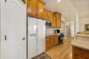 Kitchen featuring backsplash, arched walkways, built in desk, stainless steel microwave, and fridge with ice dispenser