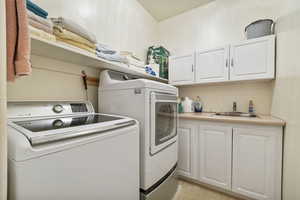 Laundry room featuring washer and clothes dryer, a sink, and cabinet space.