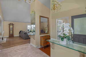 Foyer entrance with a chandelier, high vaulted ceiling, wood finished floors, and baseboards
