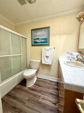 Full bathroom featuring ornamental molding, vanity, wood finished floors, toilet, and shower / bath combination with glass door