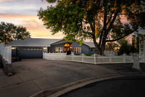 Ranch-style home featuring a fenced front yard, concrete driveway, a garage, and roof with shingles