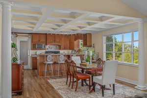 Dining area with ornate columns, coffered ceiling, light wood-style flooring, beamed ceiling, and baseboards