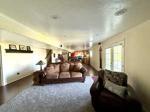 Living room featuring crown molding, stairway, baseboards, a textured ceiling, and dark wood-type flooring