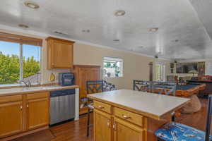 Kitchen featuring stainless steel dishwasher, a sink, a breakfast bar, dark wood-type flooring, and crown molding