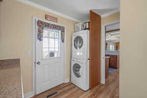 Laundry area featuring estacked washer and dryer, light wood-type flooring, ornamental molding, and baseboards