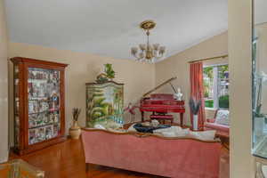 Sitting room with a chandelier, vaulted ceiling, wood finished floors, and baseboards