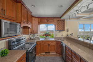 Kitchen featuring appliances with stainless steel finishes, a sink, crown molding, healthy amount of natural light, and brown cabinets
