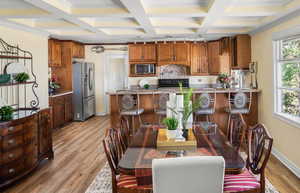 Dining space featuring coffered ceiling, light wood-type flooring, baseboards, beamed ceiling, and crown molding