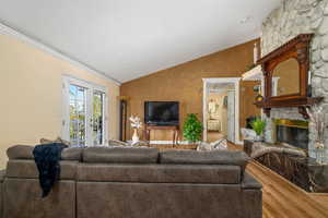 Living area with wood finished floors, vaulted ceiling, a stone fireplace, ornamental molding, and baseboards