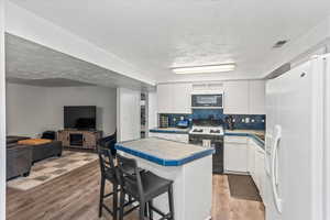 Kitchen featuring white fridge with ice dispenser, gas stove, tile counters, white cabinets, and light wood-type flooring