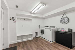 Washroom with washing machine and dryer, a textured ceiling, cabinet space, dark wood-style flooring, and baseboards