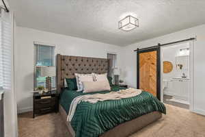 Bedroom with a barn door, carpet floors, a textured ceiling, ensuite bathroom, and a sink