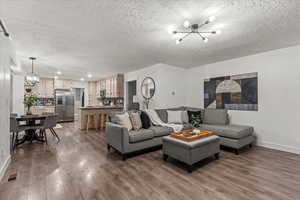 Living area featuring a chandelier, a textured ceiling, dark wood-style flooring, baseboards, and recessed lighting