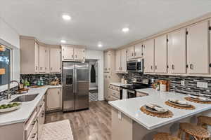 Kitchen with appliances with stainless steel finishes, a sink, a peninsula, decorative backsplash, and light wood-style floors