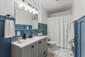 Bathroom featuring toilet, tile patterned flooring, wainscoting, vanity, and a shower with shower curtain