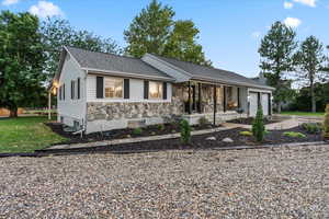 Ranch-style home with covered porch, a garage, driveway, a chimney, and stone siding