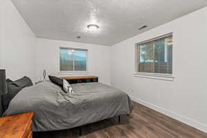 Bedroom with wood finished floors, baseboards, a textured ceiling, and multiple windows