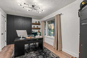Office space featuring a chandelier, light wood finished floors, baseboards, and a textured ceiling