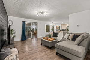 Living area featuring a chandelier, wood finished floors, baseboards, and a textured ceiling