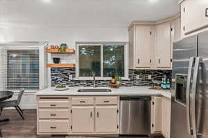 Kitchen with stainless steel appliances, a sink, light countertops, tasteful backsplash, and dark wood-style floors