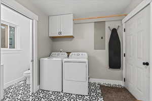 Washroom with electric panel, cabinet space, baseboards, washer and dryer, and a textured ceiling