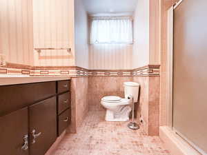 Full bathroom featuring wallpapered walls, toilet, a shower with door, a wainscoted wall, and tile patterned flooring