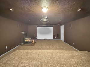 Cinema with carpet flooring, a wood stove, baseboards, a textured ceiling, and recessed lighting