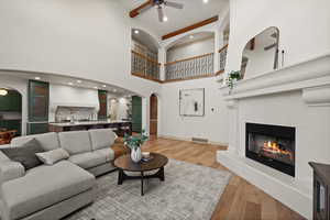 Living area with a ceiling fan, a high ceiling, arched walkways, light wood-style flooring, and a glass covered fireplace