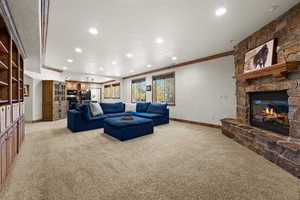 Living room with light carpet, crown molding, recessed lighting, a stone fireplace, and baseboards