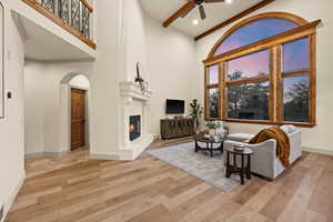 Living area featuring wood finished floors, ceiling fan, a large fireplace, baseboards, and a high ceiling