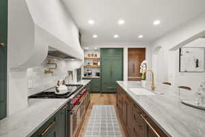 Kitchen featuring high quality appliances, a sink, green cabinets, recessed lighting, and decorative backsplash