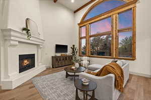 Living room with a towering ceiling, a glass covered fireplace, wood finished floors, beamed ceiling, and baseboards