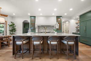 Kitchen featuring green cabinetry, arched walkways, backsplash, light stone counters, and recessed lighting
