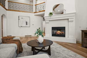 Living area with wood finished floors, a glass covered fireplace, arched walkways, a high ceiling, and baseboards