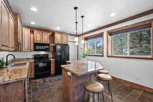 Kitchen with black appliances, a sink, a center island, a kitchen bar, and light stone counters