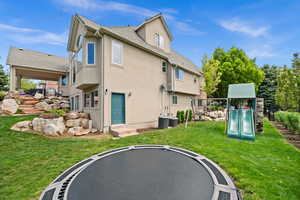 Back of house featuring stucco siding, a trampoline, a playground, a yard, and central AC unit