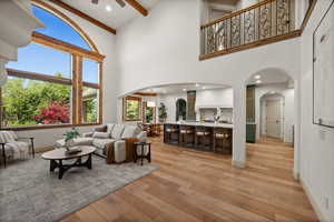 Living area with arched walkways, a towering ceiling, a ceiling fan, light wood-style flooring, and beam ceiling