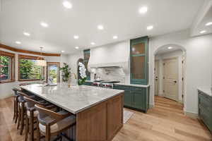 Kitchen featuring green cabinets, recessed lighting, decorative backsplash, arched walkways, and an island with sink