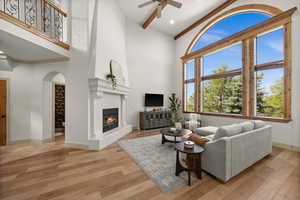 Living area featuring a large fireplace, a ceiling fan, wood finished floors, arched walkways, and baseboards