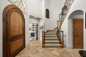 Entrance foyer featuring arched walkways, a high ceiling, stairway, baseboards, and stone tile flooring
