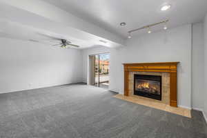 Unfurnished living room featuring carpet flooring, rail lighting, ceiling fan, and a tiled fireplace
