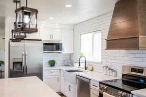 Kitchen with stainless steel appliances, tasteful backsplash, white cabinets, light countertops, and a textured ceiling