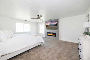 Bedroom with light carpet, a fireplace, a ceiling fan, and a textured ceiling
