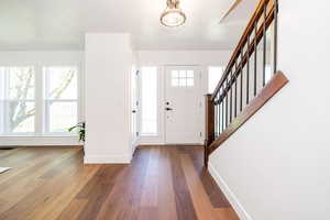 Foyer entrance featuring baseboards, wood finished floors, stairway, and plenty of natural light
