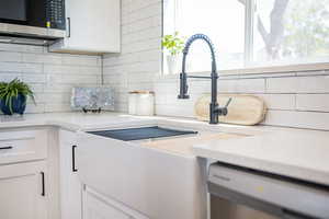 Kitchen view of stainless steel microwave, dishwashing machine, and tasteful backsplash