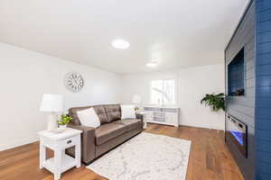 Living room featuring a large fireplace, wood finished floors, and baseboards
