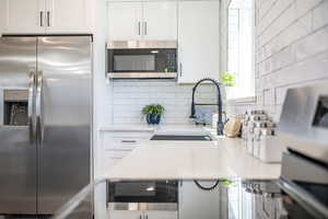 Kitchen with stainless steel appliances, light stone countertops, white cabinets, and decorative backsplash