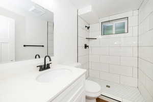 Full bathroom with toilet, tiled shower, and vanity